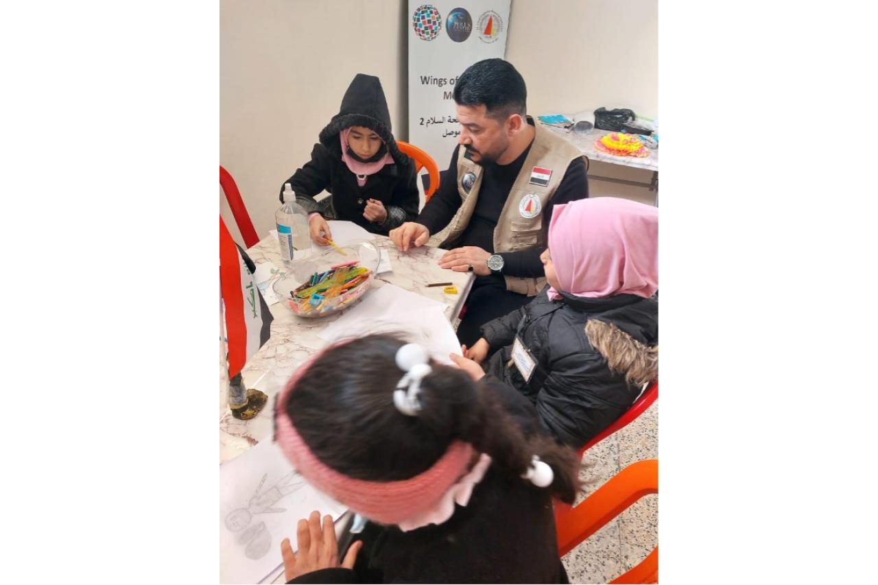 Staff member of Al-Ghad seated, overseeing three children who are drawing and painting