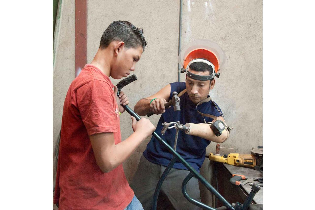 Two men with prosthetics in workshop building a wheelchair (photo by Stephen Petegorsky)