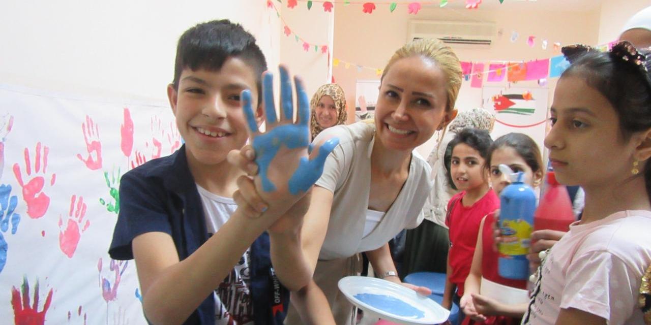 Syrian refugee boy with paint on his and and Dr. Niveen Abuzaid smiling at the Sir Bobby Charlton Centre in Amman, Jordan as part of the Polus Center's Wings of Peace program. 